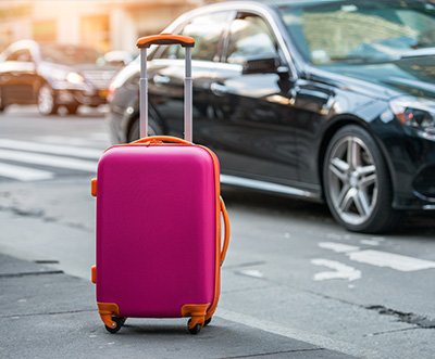 a vibrant pink suitcase with orange accents on a city street near cars ready for travel and adventure with nine travel essentials
