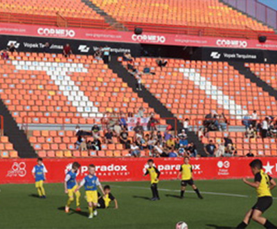 children playing soccer on a field during a match with spectators in the background and colorful stadium seating showcasing three teams in action