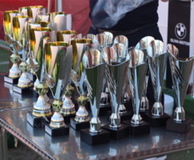 a collection of shiny trophies on a table with a person holding one trophy in the background celebrating six accomplishments or achievements