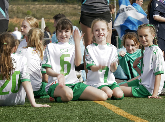 young girls at a soccer game smiling and showing jersey number 6 with teammates in sports attire sitting on a field enjoying the team spirit and camaraderie