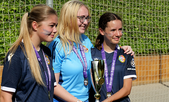 three young female soccer players celebrating with a trophy featuring a first place win in a tournament representing 7 athletes